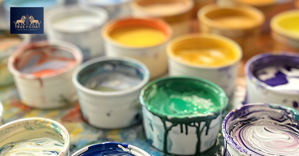 Array of professional paint cans, primer containers, and painting supplies arranged neatly on drop cloth, showing variety of products used in exterior painting, bright lighting, no text on image